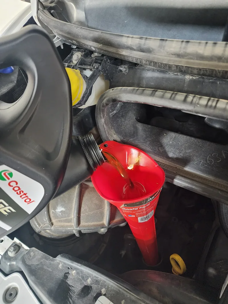 Fresh engine oil being poured through a funnel during a mobile oil change
