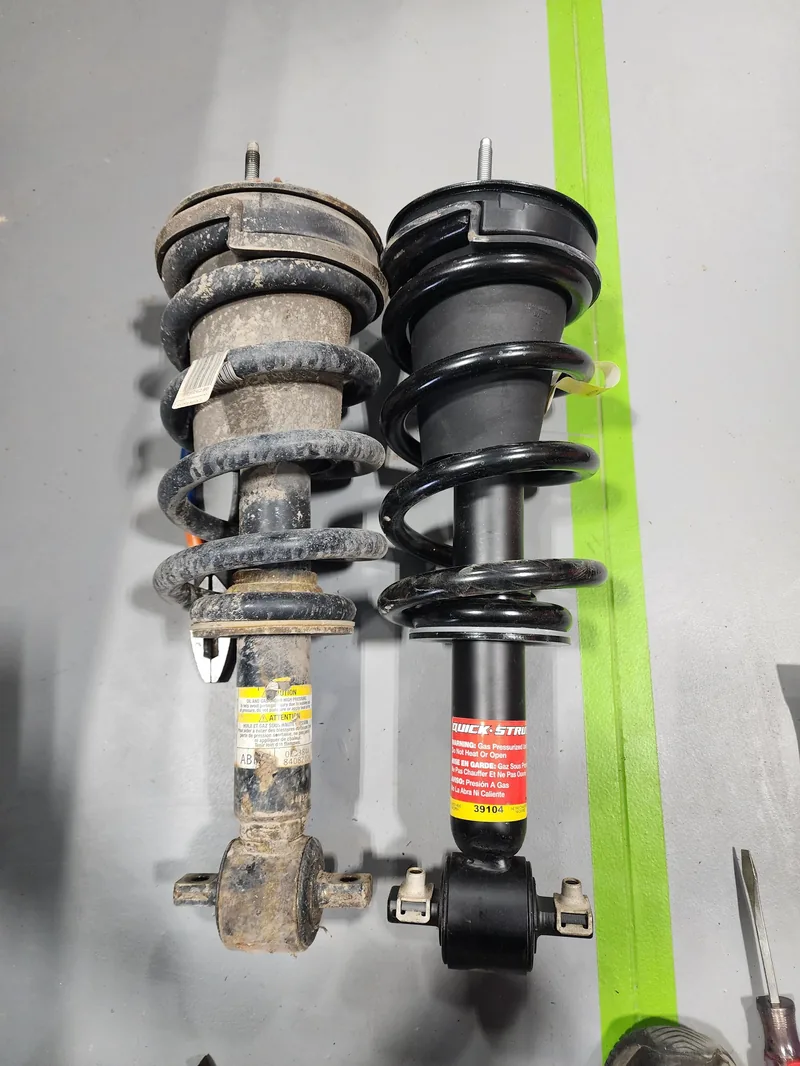Worn factory strut assembly beside a new replacement strut ready for installation