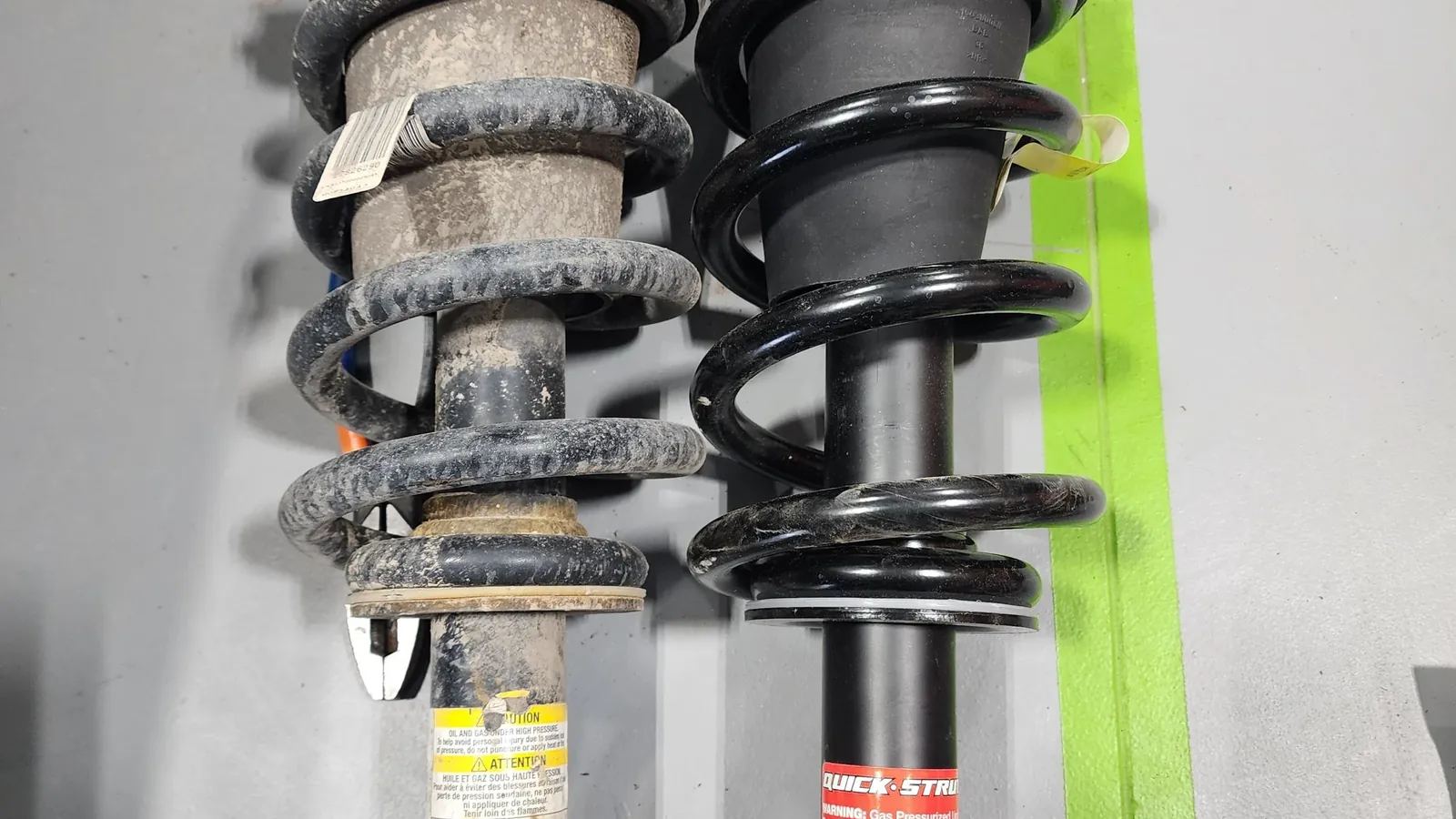 Worn factory strut assembly beside a new replacement strut ready for installation