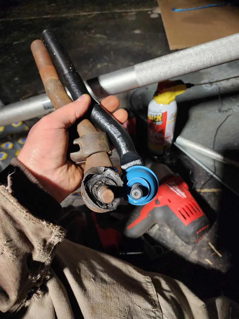 Technician holding a replacement tie rod end beside a cordless impact wrench