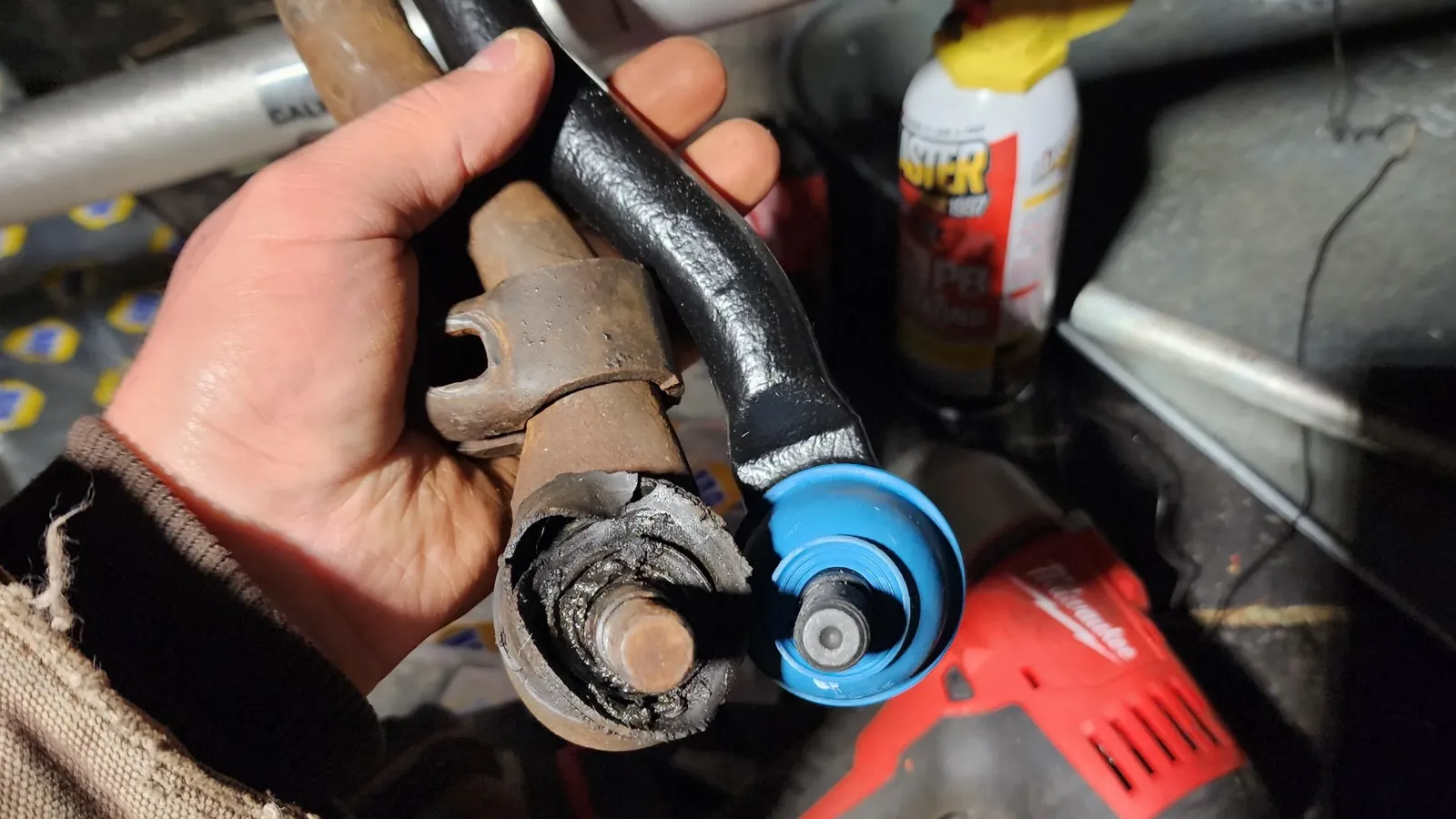 Technician holding a replacement tie rod end beside a cordless impact wrench